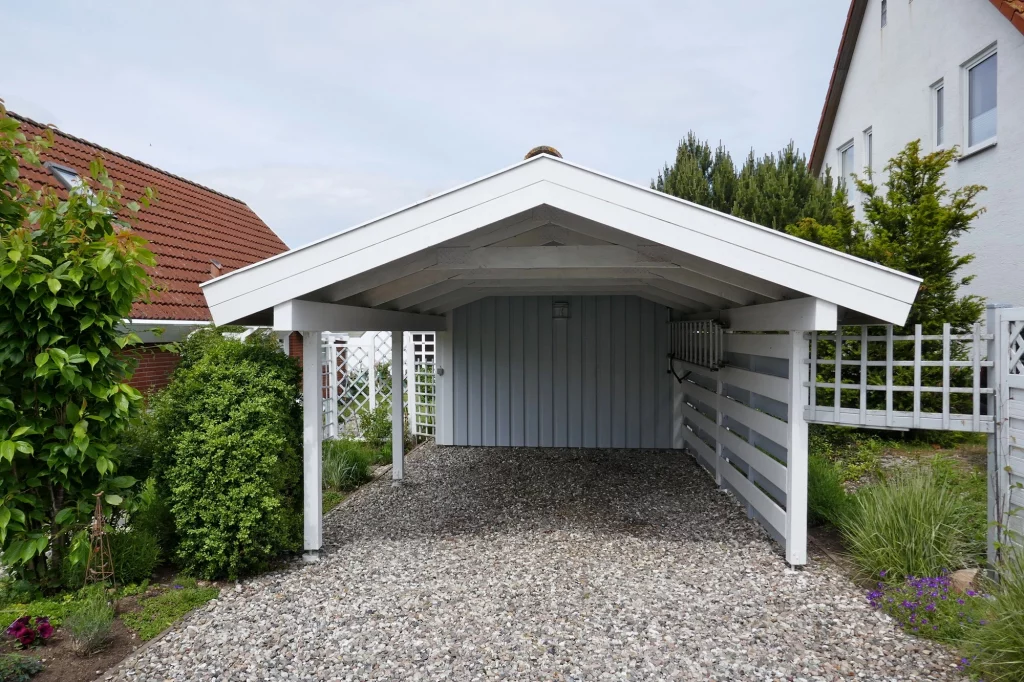 Freistehendes Carport in Eschborn, nahe Frankfurt am Main. Getragen von vier Säulen, präsentiert sich das Dach in einem Winkel von 30 Grad. Die charakteristische Rückwand des Carports erstrahlt in hellem Blau, während der Rest in frischem Weiß gestrichen ist. Ein harmonisches Zusammenspiel von Farben und Formen für stilvollen Fahrzeugschutz.